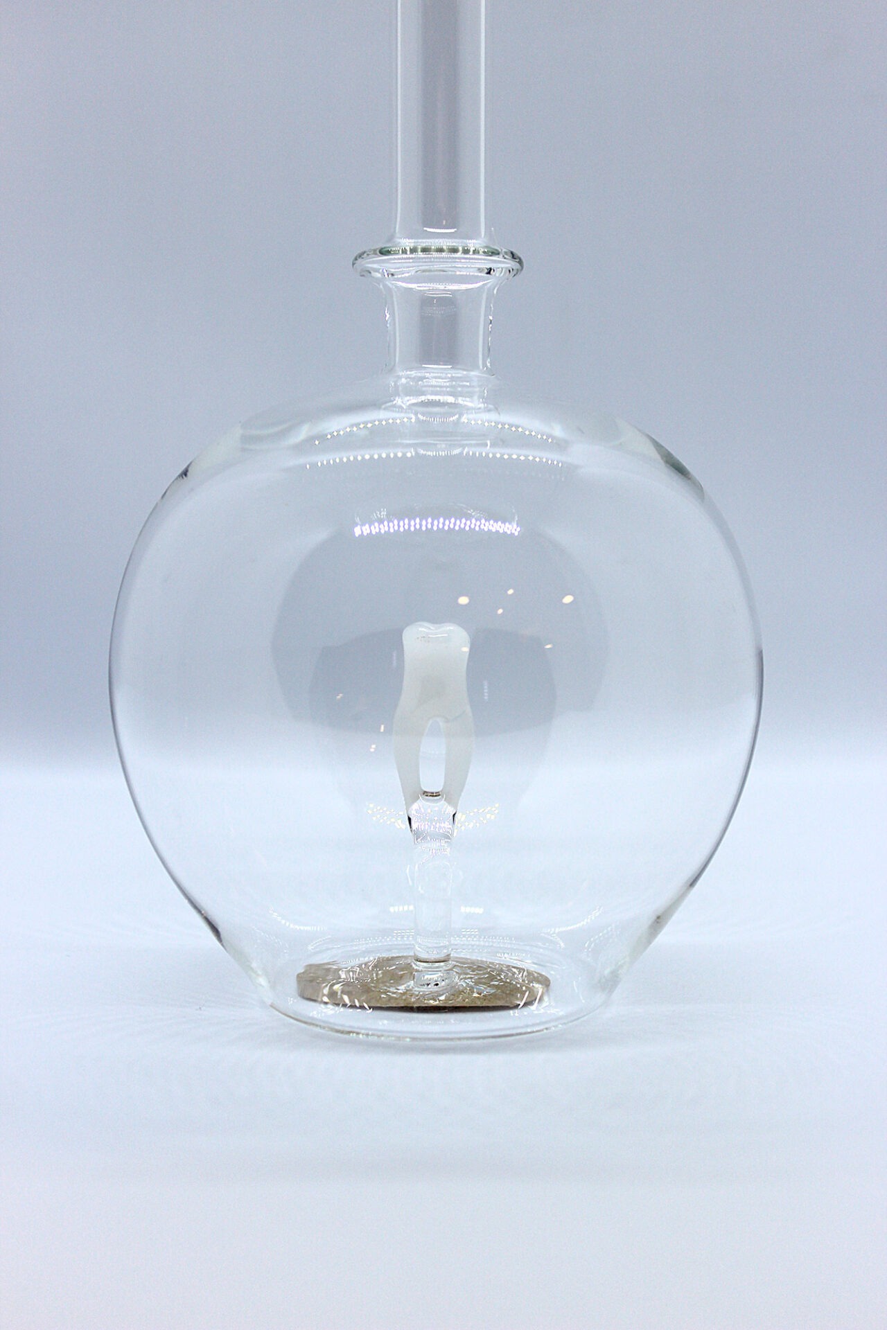 Eine leere bauchige Flasche aus Glas mit einem aus Glas geblasenen Zahn im Inneren.