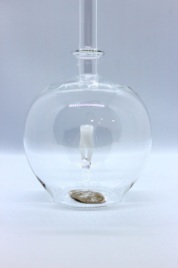 Eine leere bauchige Flasche aus Glas mit einem aus Glas geblasenen Zahn im Inneren.