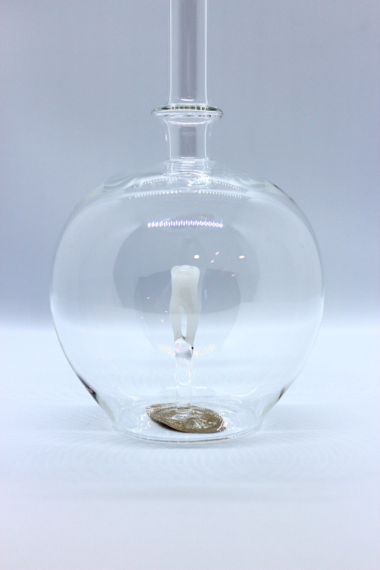 Eine leere bauchige Flasche aus Glas mit einem aus Glas geblasenen Zahn im Inneren.