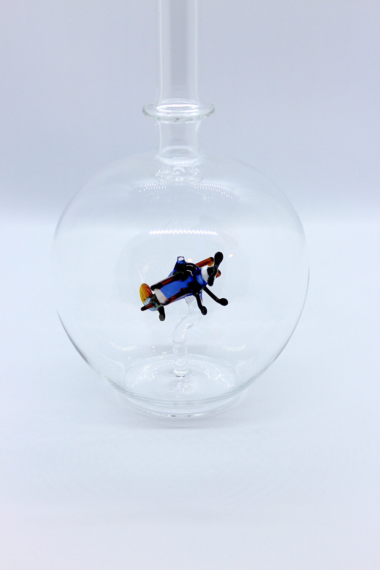 Eine leere bauchige Flasche aus Glas mit einem aus Glas geblasenen Doppeldecker im Inneren.