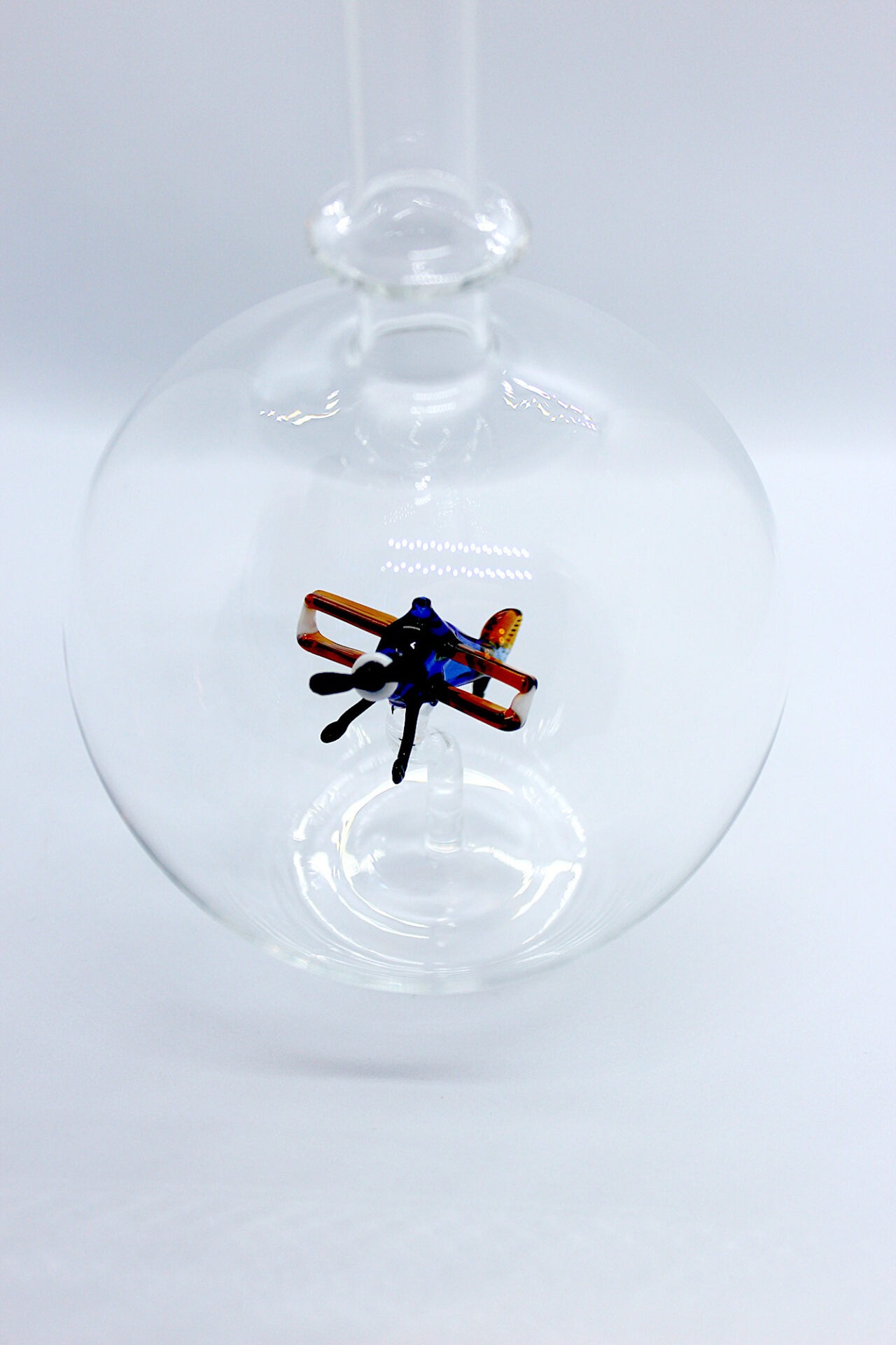 Eine leere bauchige Flasche aus Glas mit einem aus Glas geblasenen Doppeldecker im Inneren.