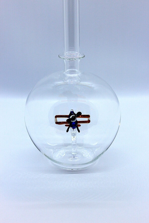 Eine leere bauchige Flasche aus Glas mit einem aus Glas geblasenen Doppeldecker im Inneren.