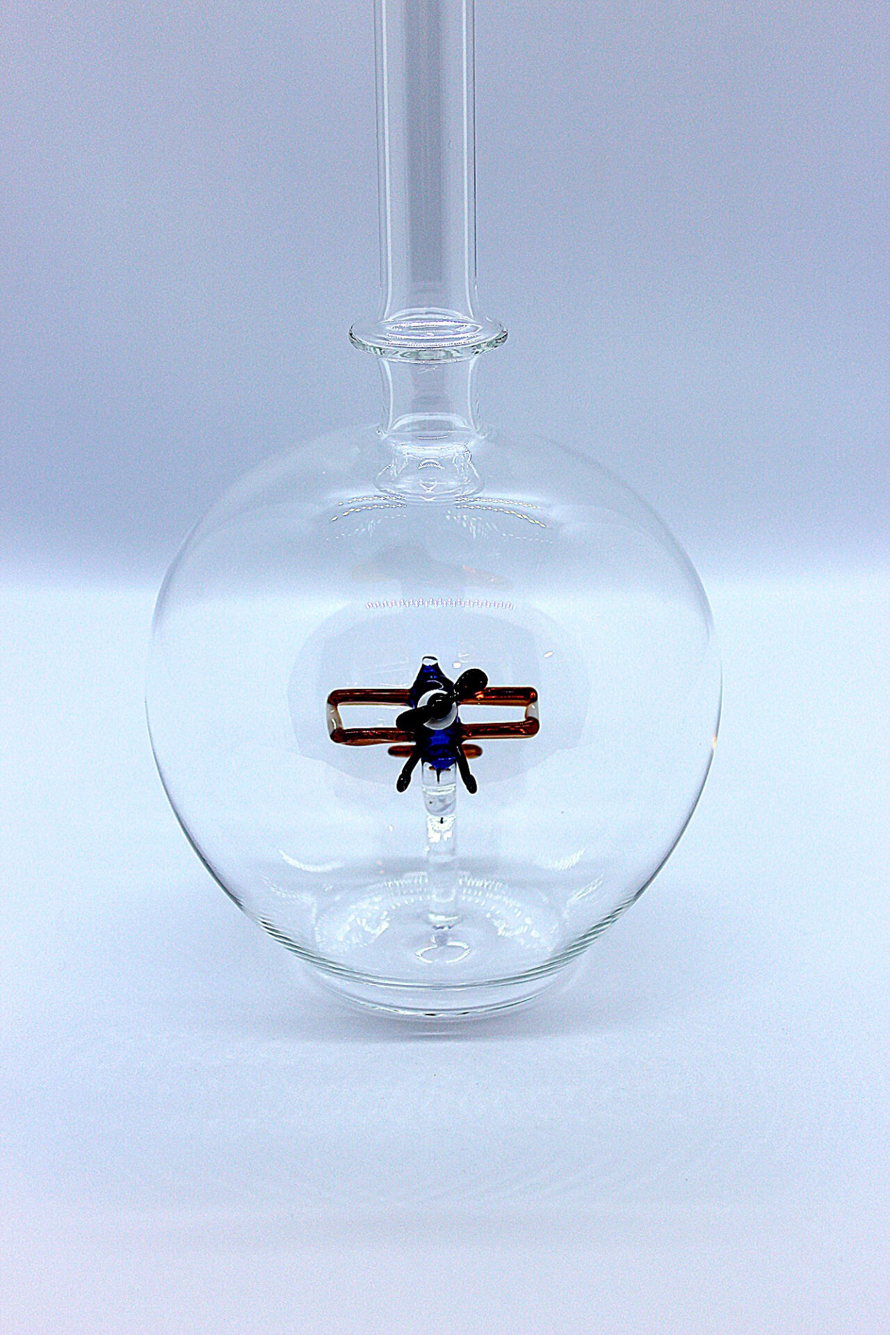 Eine leere bauchige Flasche aus Glas mit einem aus Glas geblasenen Doppeldecker im Inneren.