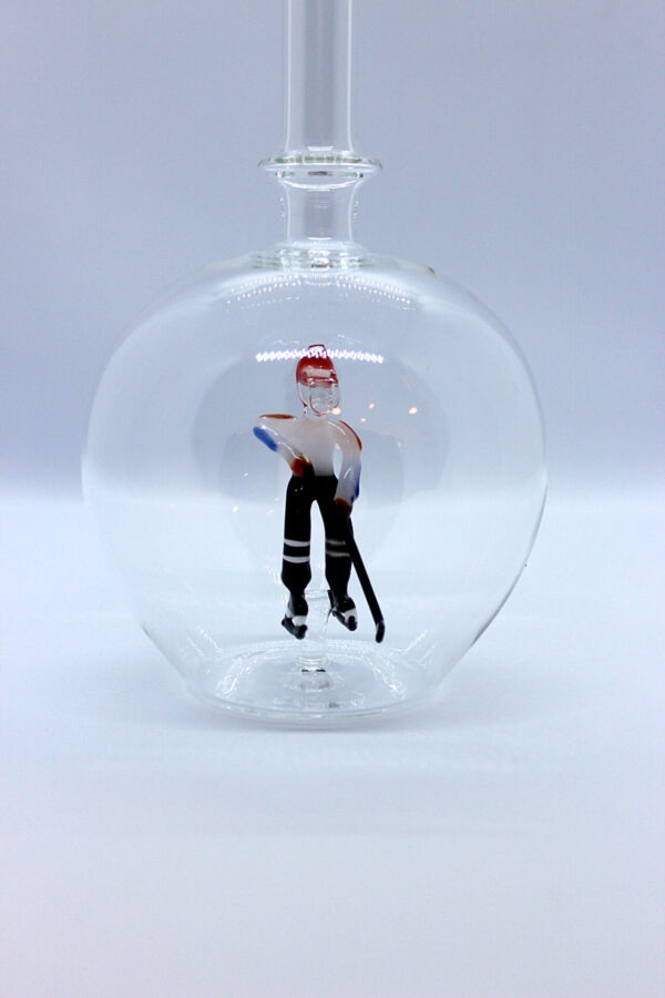 Eine leere bauchige Flasche aus Glas mit einem aus Glas geblasenen Eishockeyspieler im Inneren.