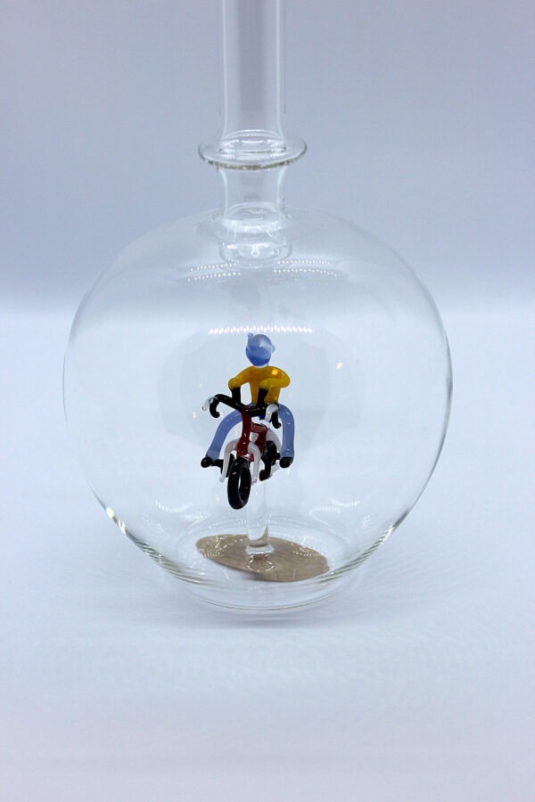 Eine leere bauchige Flasche aus Glas mit einem aus Glas geblasenen Radfahrer im Inneren.