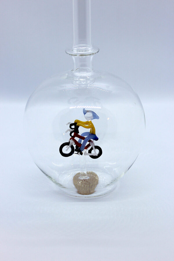 Eine leere bauchige Flasche aus Glas mit einem aus Glas geblasenen Radfahrer im Inneren.