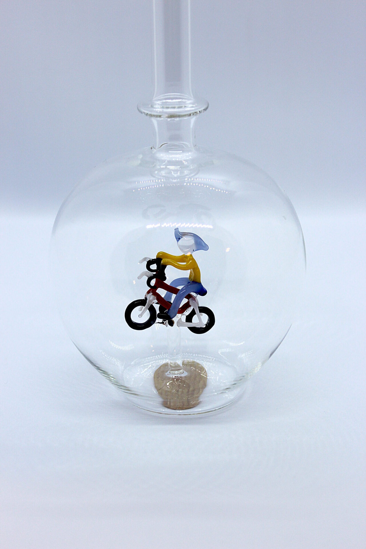 Eine leere bauchige Flasche aus Glas mit einem aus Glas geblasenen Radfahrer im Inneren.