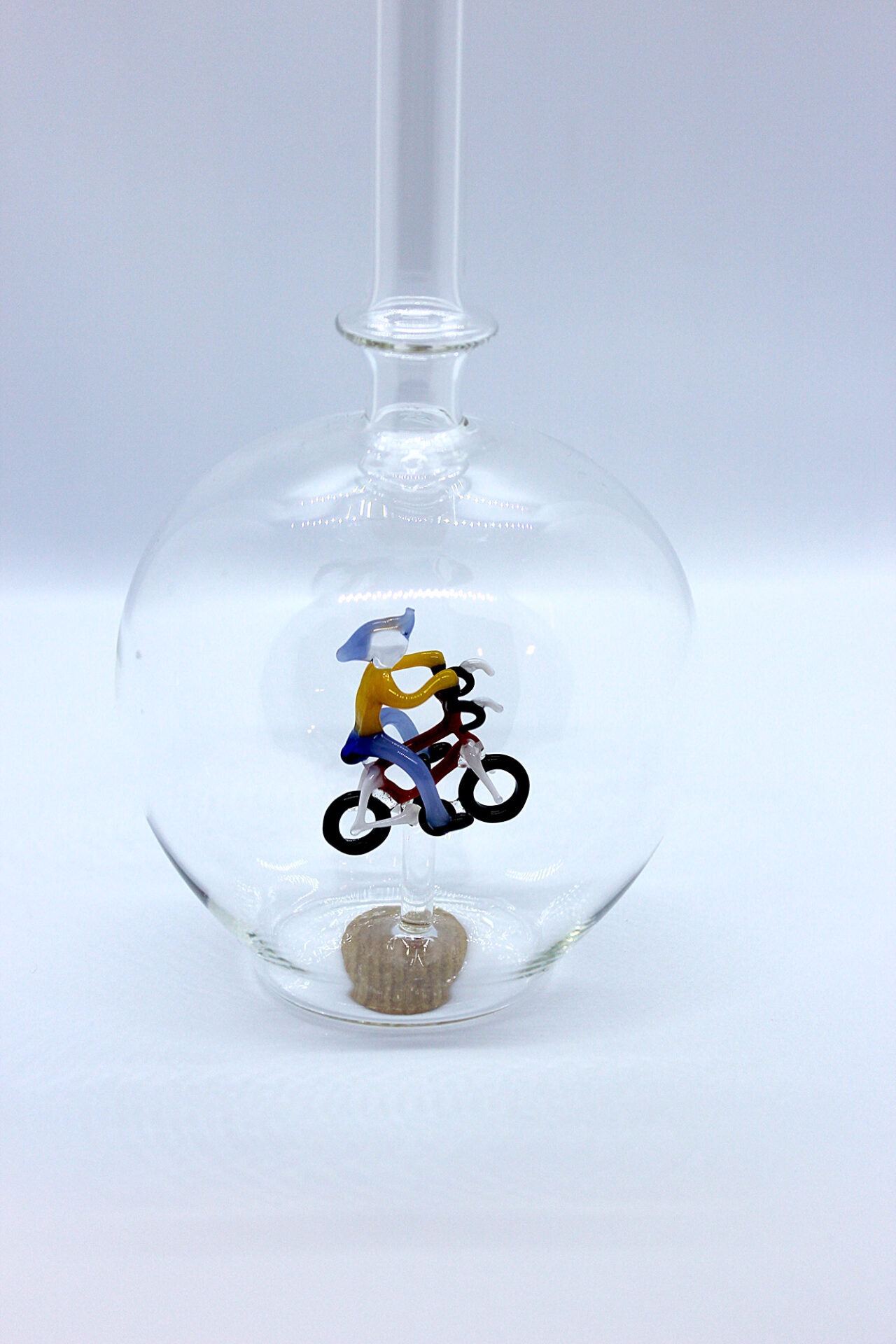 Eine leere bauchige Flasche aus Glas mit einem aus Glas geblasenen Radfahrer im Inneren.