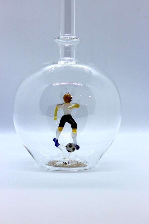 Eine leere bauchige Flasche aus Glas mit einem aus Glas geblasenen Fußballspieler im Inneren.