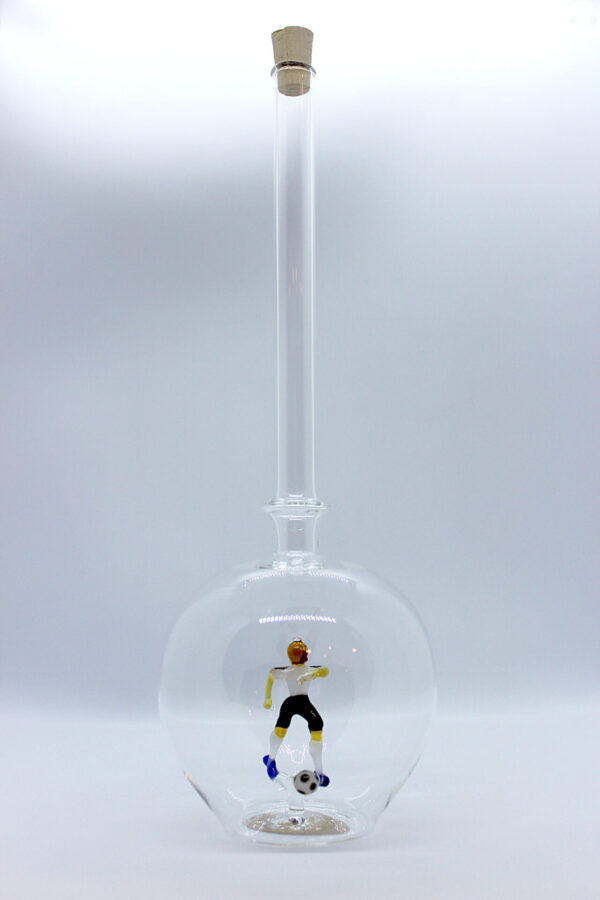 Eine leere bauchige Flasche aus Glas mit einem aus Glas geblasenen Fußballspieler im Inneren.