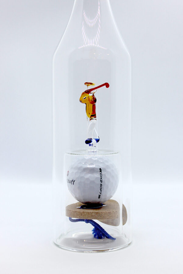 Eine leere längliche Flasche aus Glas mit einem aus Glas geblasenen Golfspieler und einem Golfball im Inneren.