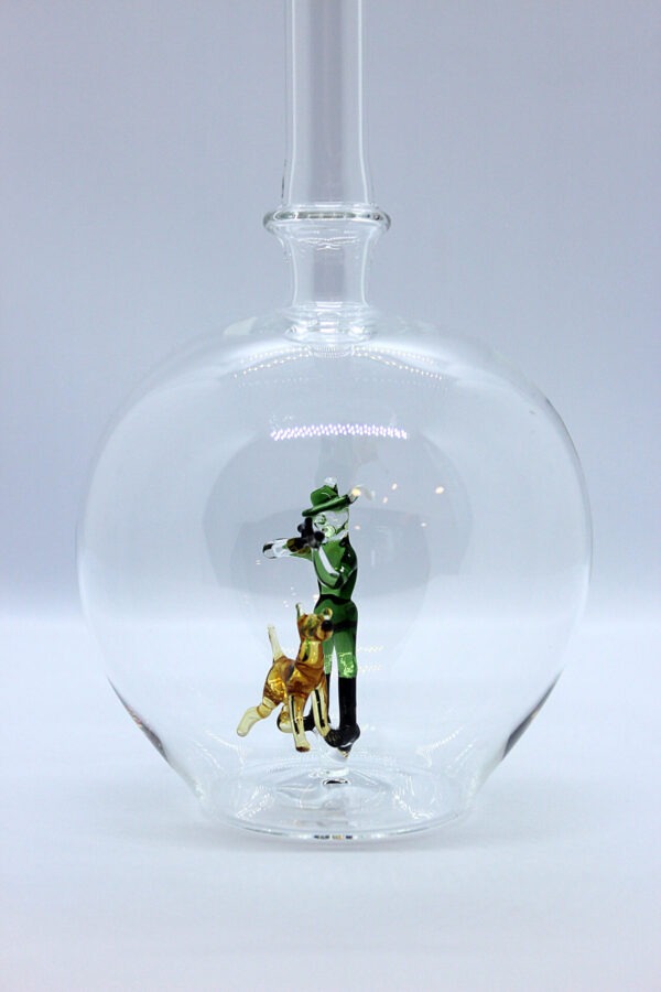 Eine leere bauchige Flasche aus Glas mit einem aus Glas geblasenen Jäger mit Hund im Inneren.