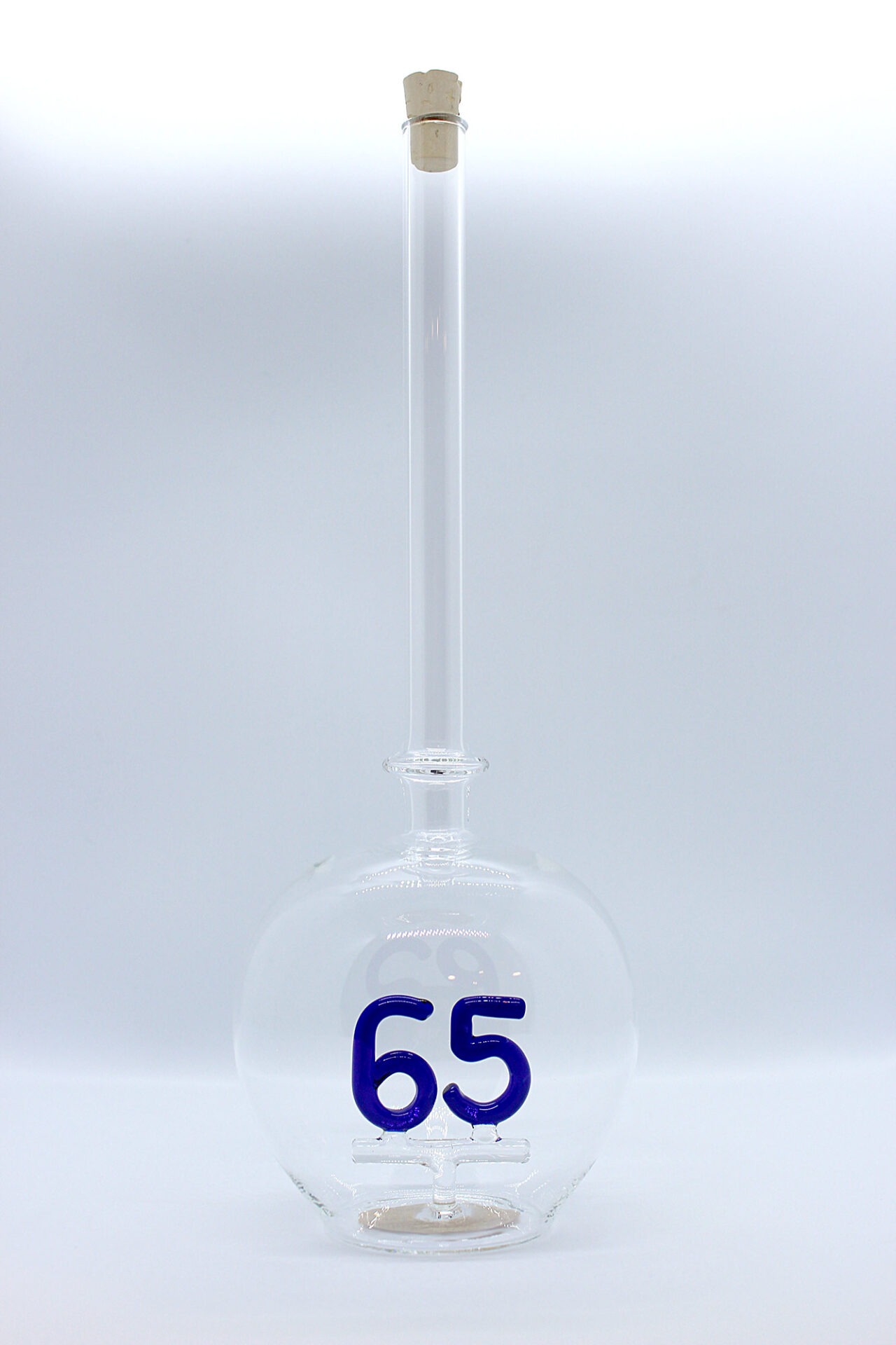 Eine leere bauchige Flasche aus Glas mit einer aus Glas geblasenen Zahl 65 im Inneren.