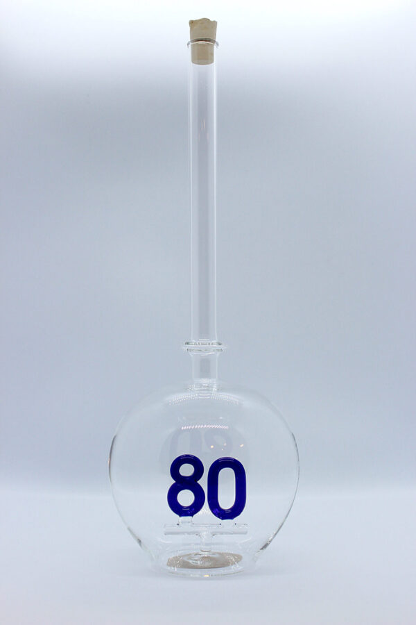 Eine leere bauchige Flasche aus Glas mit einer aus Glas geblasenen Zahl 80 im Inneren.