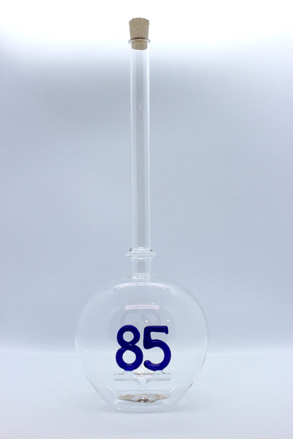 Eine leere bauchige Flasche aus Glas mit einer aus Glas geblasenen Zahl 85 im Inneren.