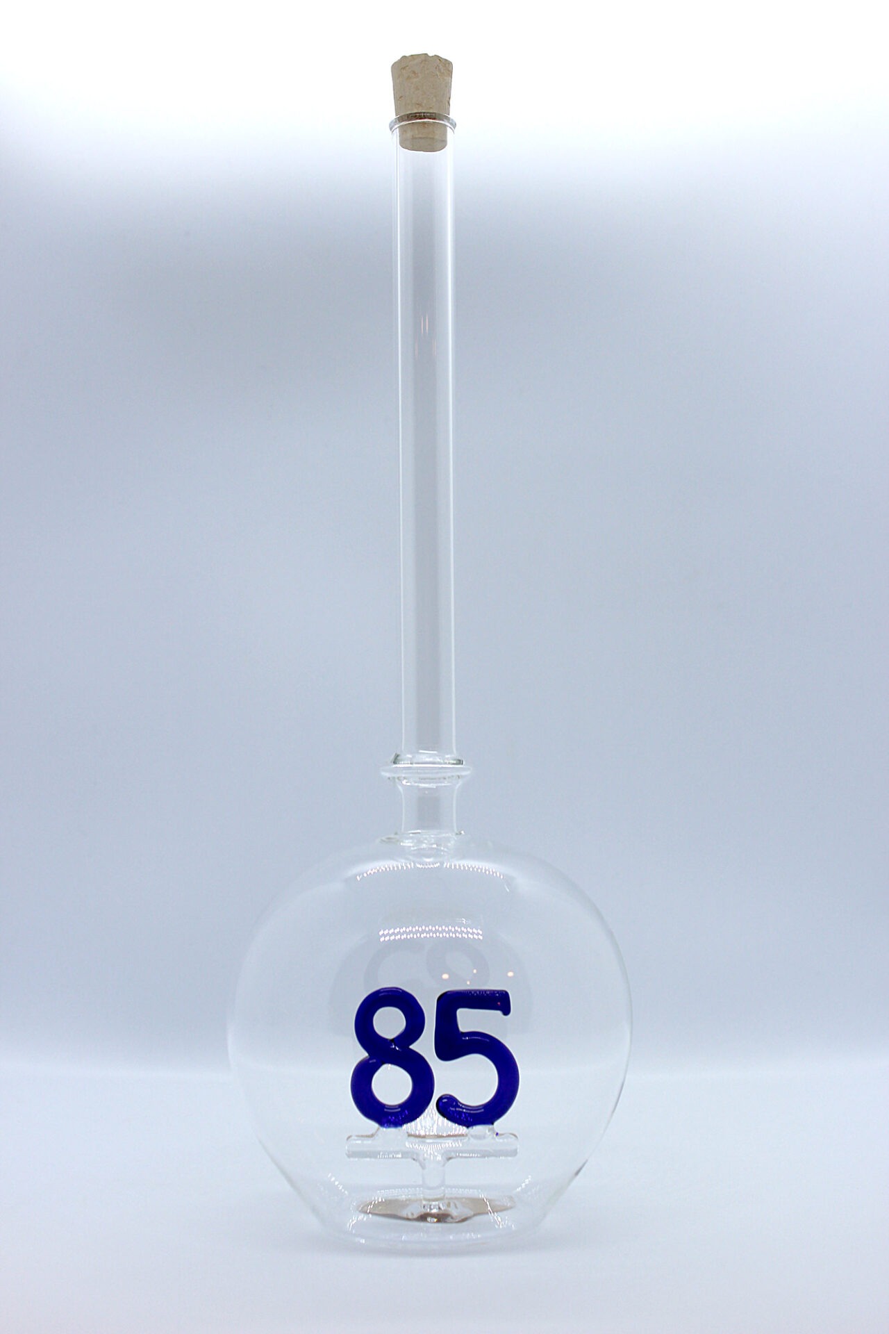 Eine leere bauchige Flasche aus Glas mit einer aus Glas geblasenen Zahl 85 im Inneren.