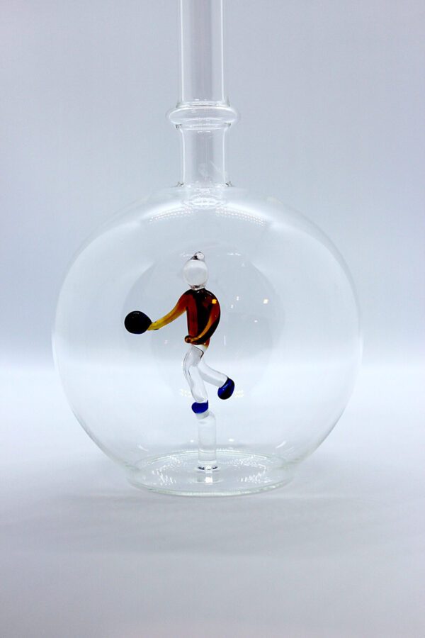 Eine leere bauchige Flasche aus Glas mit einem aus Glas geblasenen Kegelspieler im Inneren.