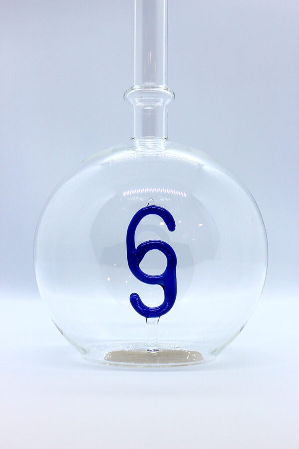 Eine leere bauchige Flasche aus Glas mit einem aus Glas geblasenen Paragraphen-Zeichen im Inneren.