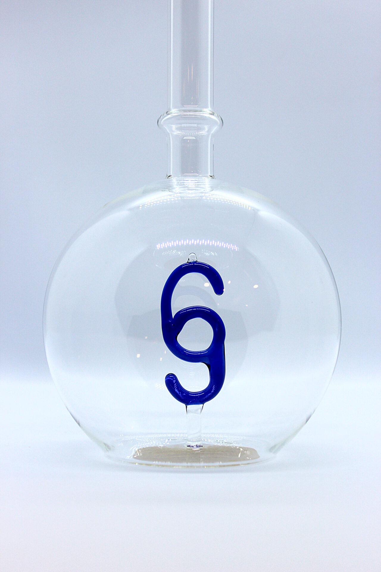 Eine leere bauchige Flasche aus Glas mit einem aus Glas geblasenen Paragraphen-Zeichen im Inneren.