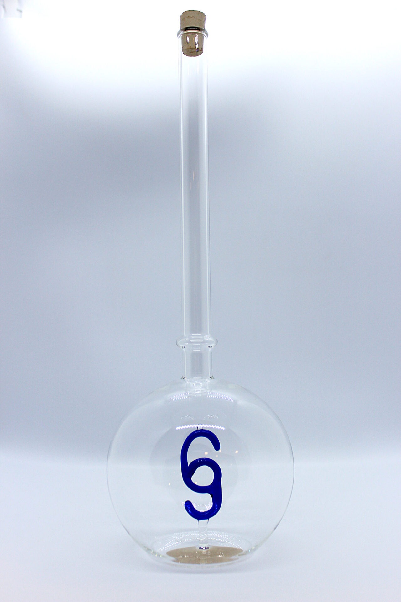 Eine leere bauchige Flasche aus Glas mit einem aus Glas geblasenen Paragraphen-Zeichen im Inneren.