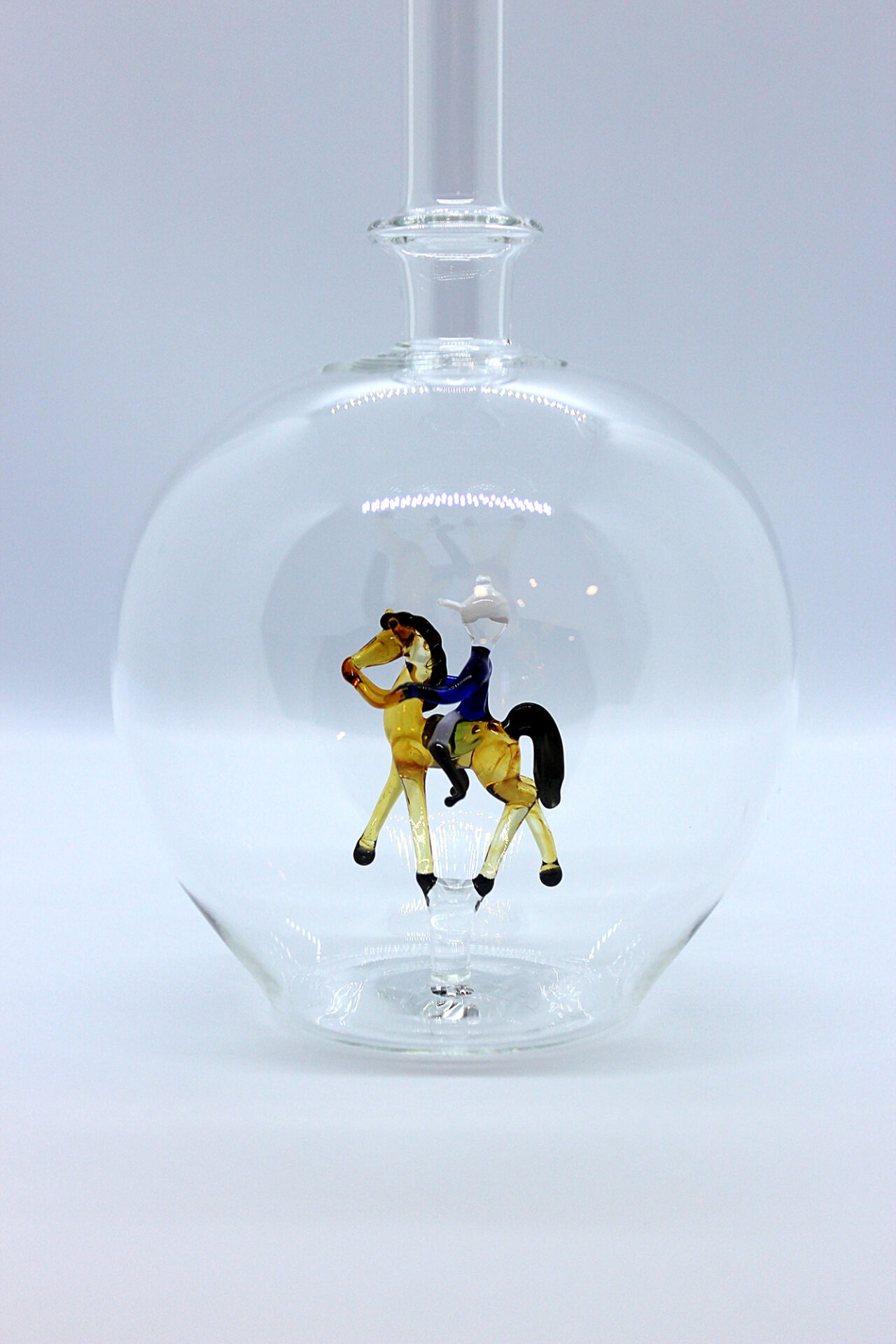 Eine leere bauchige Flasche aus Glas mit einem aus Glas geblasenen Reiter auf einem Pferd im Inneren.