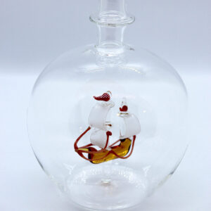 Eine leere bauchige Flasche aus Glas mit einem aus Glas geblasenen Segelschiff im Inneren.
