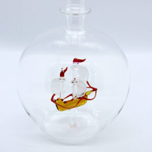 Eine leere bauchige Flasche aus Glas mit einem aus Glas geblasenen Segelschiff im Inneren.