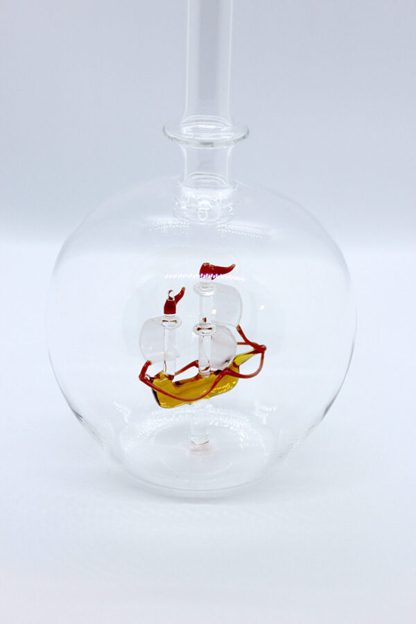 Eine leere bauchige Flasche aus Glas mit einem aus Glas geblasenen Segelschiff im Inneren.