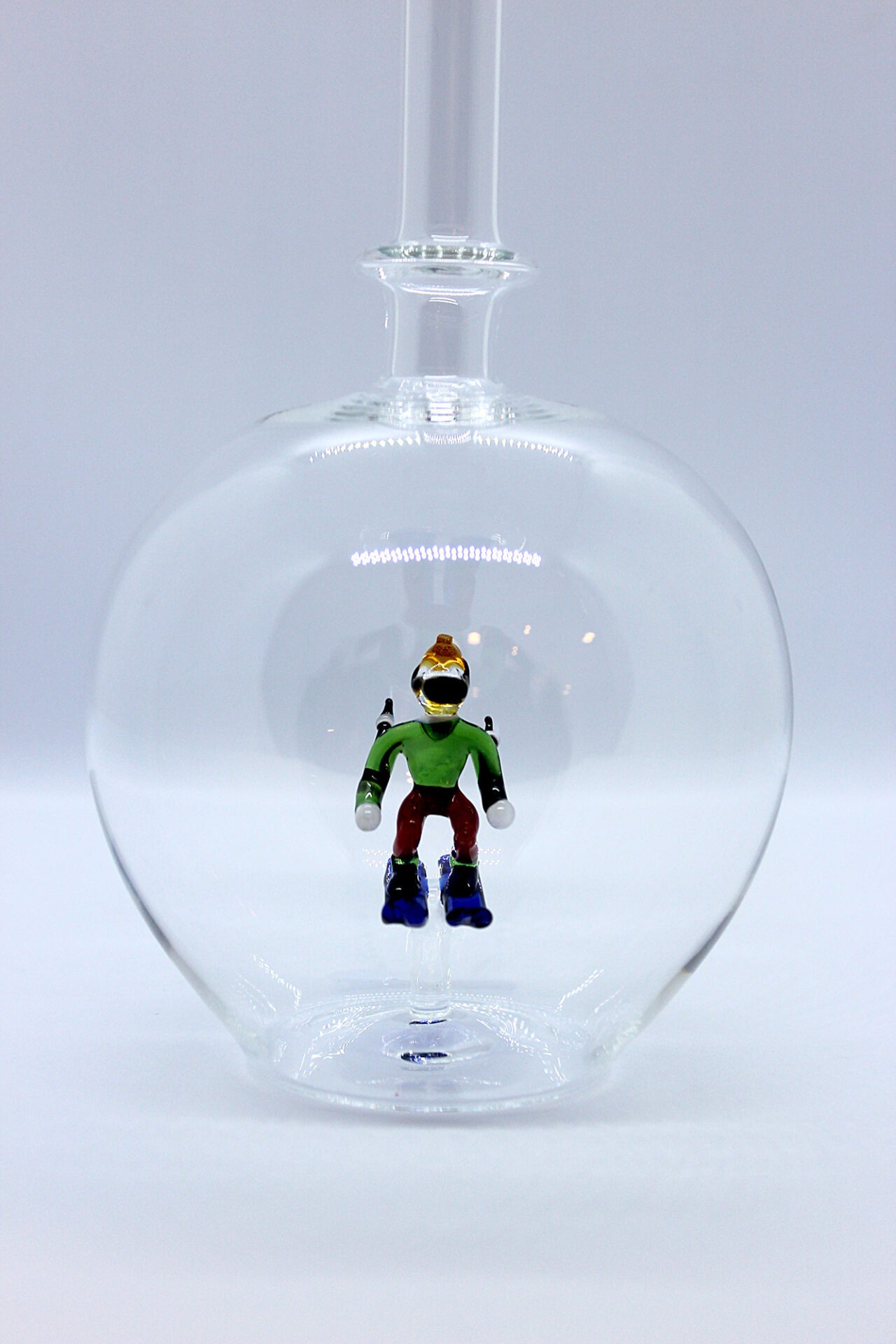 Eine leere bauchige Flasche aus Glas mit einem aus Glas geblasenen Skifahrer im Inneren.