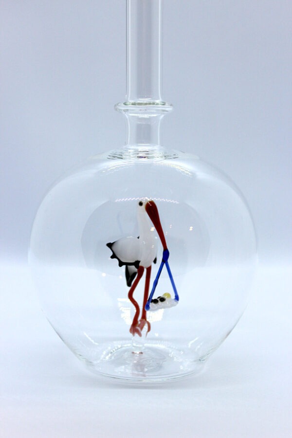 Eine leere bauchige Flasche aus Glas mit einem aus Glas geblasenen Storch mit Baby im Inneren.