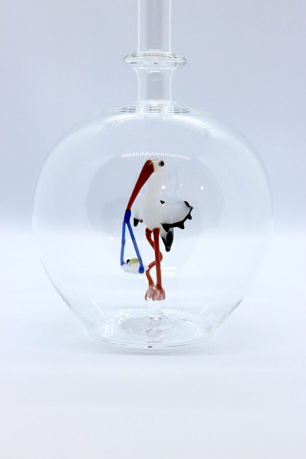Eine leere bauchige Flasche aus Glas mit einem aus Glas geblasenen Storch mit Baby im Inneren.