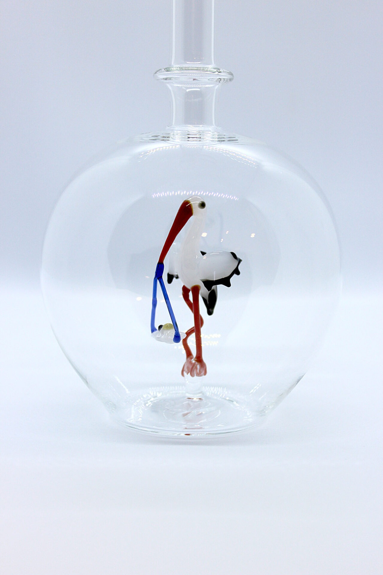 Eine leere bauchige Flasche aus Glas mit einem aus Glas geblasenen Storch mit Baby im Inneren.