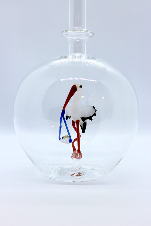 Eine leere bauchige Flasche aus Glas mit einem aus Glas geblasenen Storch mit Baby im Inneren.