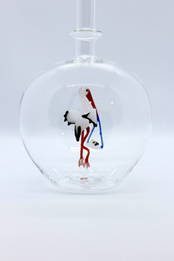 Eine leere bauchige Flasche aus Glas mit einem aus Glas geblasenen Storch mit Baby im Inneren.