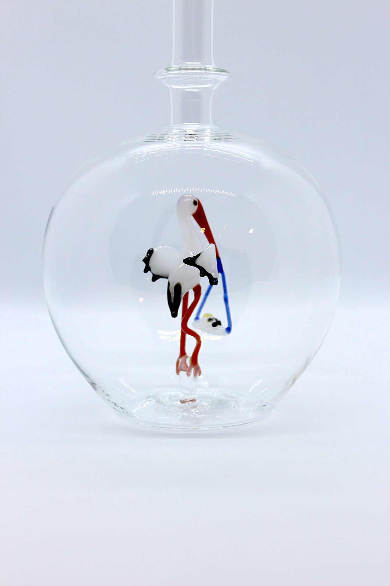 Eine leere bauchige Flasche aus Glas mit einem aus Glas geblasenen Storch mit Baby im Inneren.
