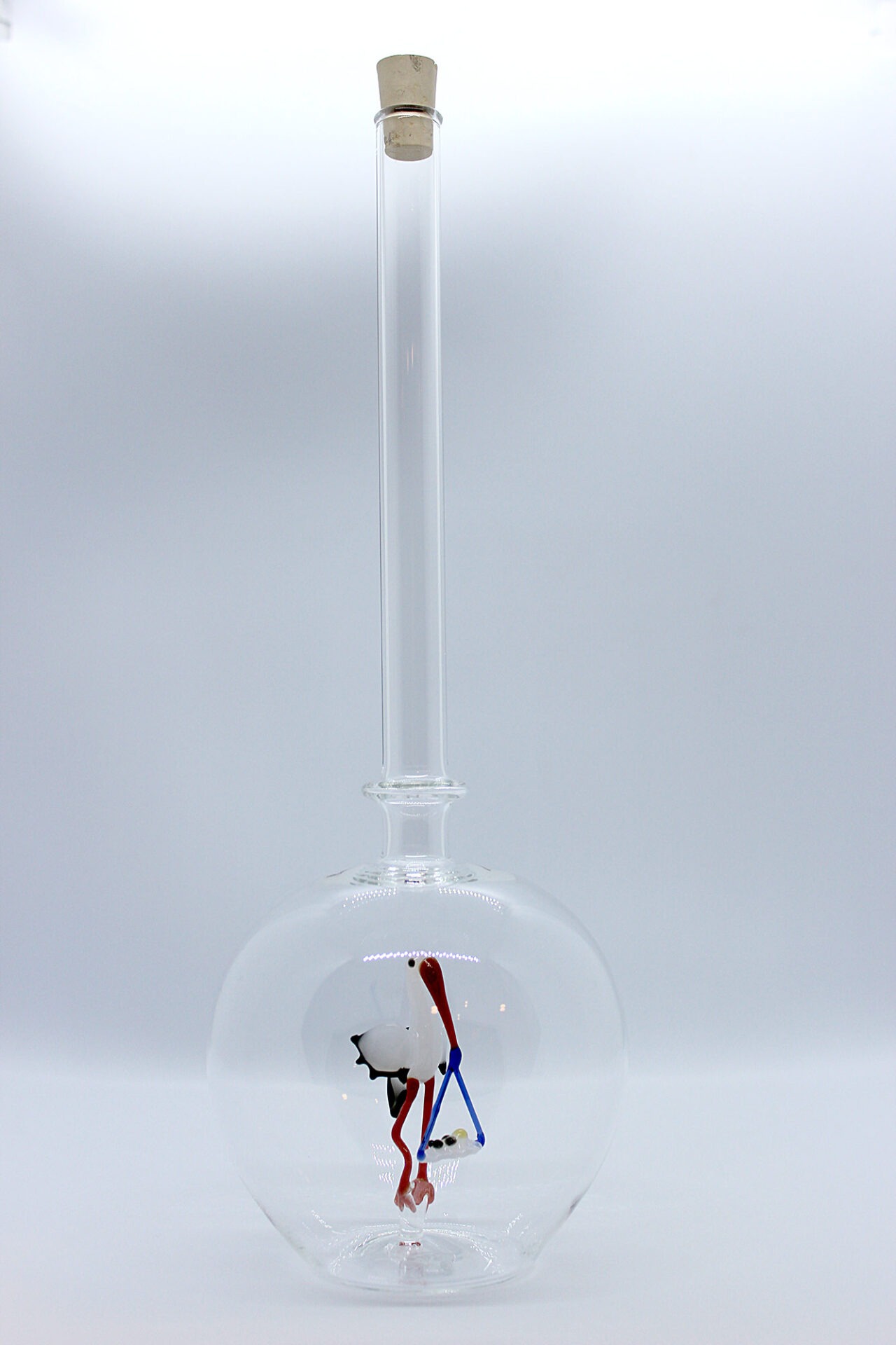 Eine leere bauchige Flasche aus Glas mit einem aus Glas geblasenen Storch mit Baby im Inneren.
