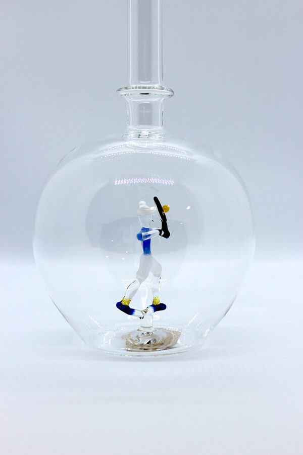 Eine leere bauchige Flasche aus Glas mit einem aus Glas geblasenen Tennisspieler im Inneren.