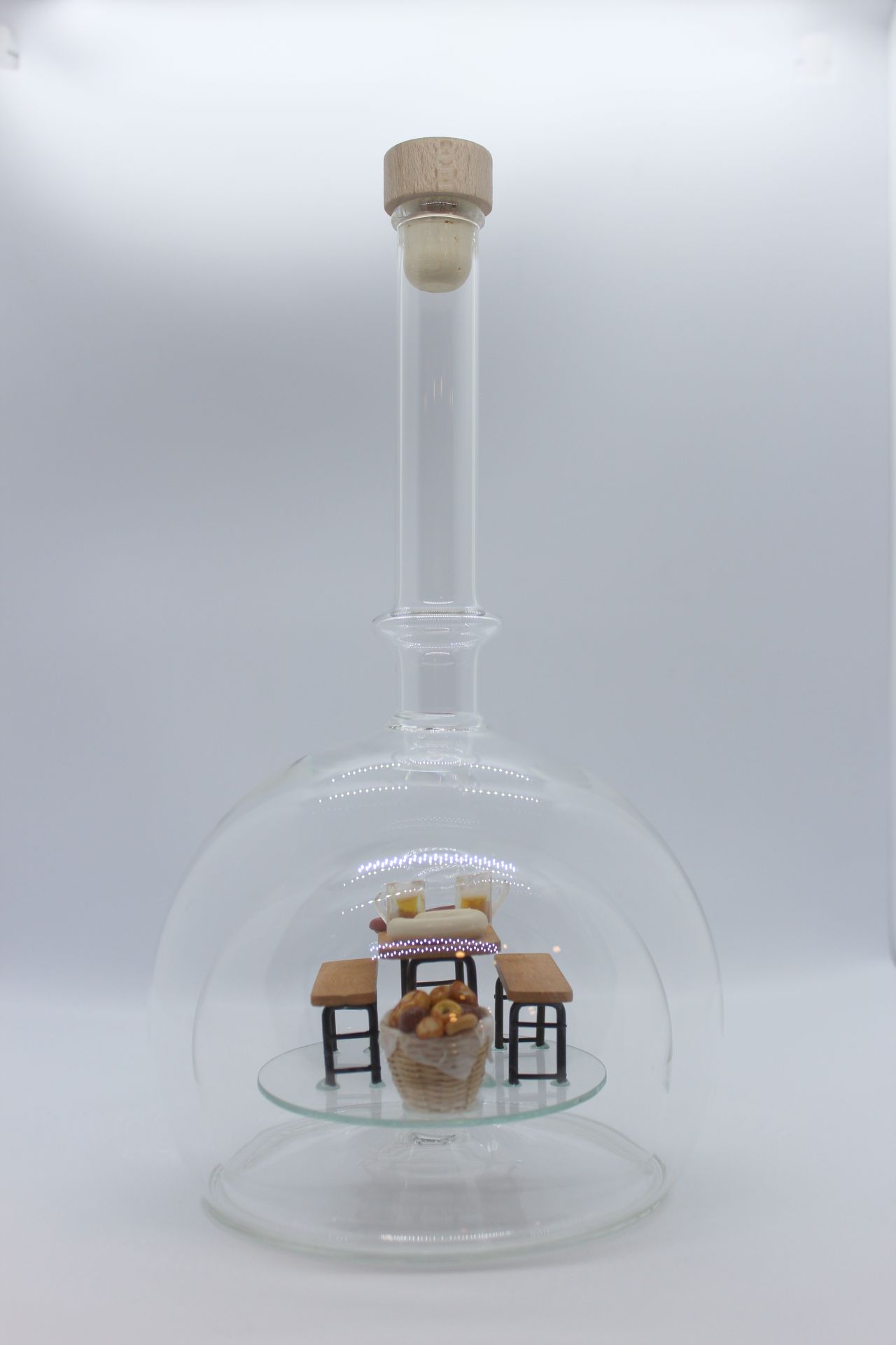 Eine leere bauchige Flasche aus Glas mit einer Bierzeltgarnitur im Inneren.