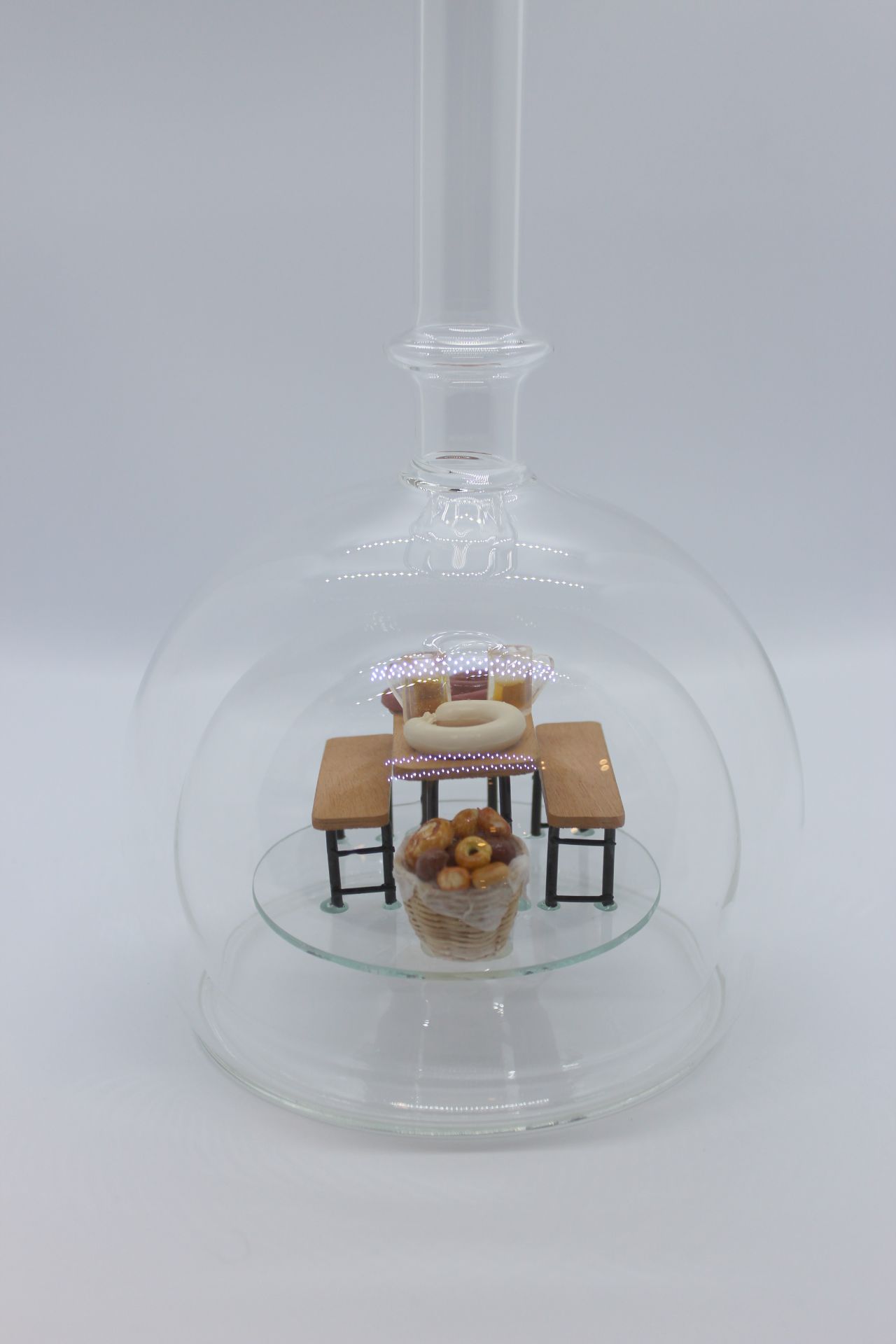 Eine leere bauchige Flasche aus Glas mit einer Bierzeltgarnitur im Inneren.