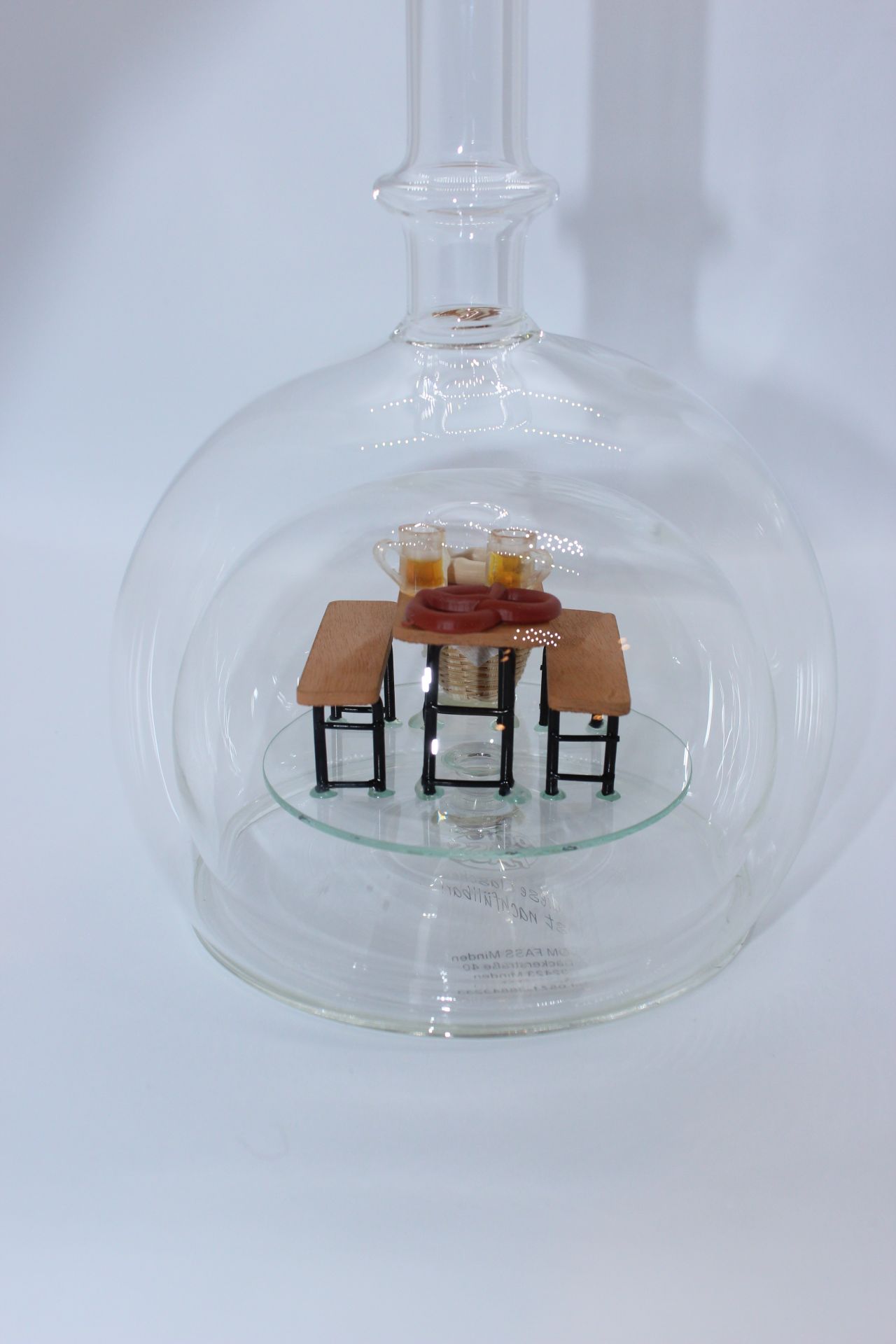 Eine leere bauchige Flasche aus Glas mit einer Bierzeltgarnitur im Inneren.