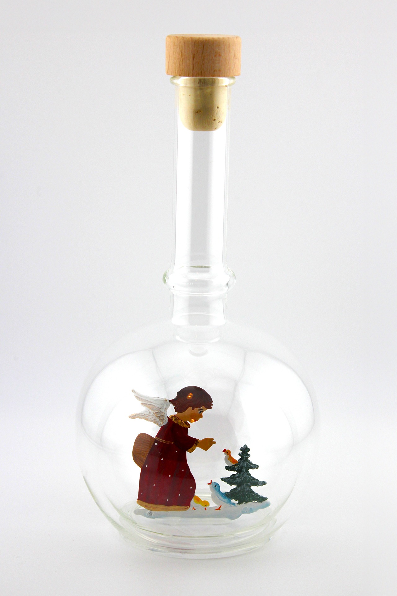 Eine leere bauchige Flasche aus Glas mit einem Vögel fütternden Engel am Tannenbaum im Inneren.