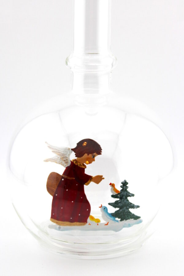 Eine leere bauchige Flasche aus Glas mit einem Vögel fütternden Engel am Tannenbaum im Inneren.