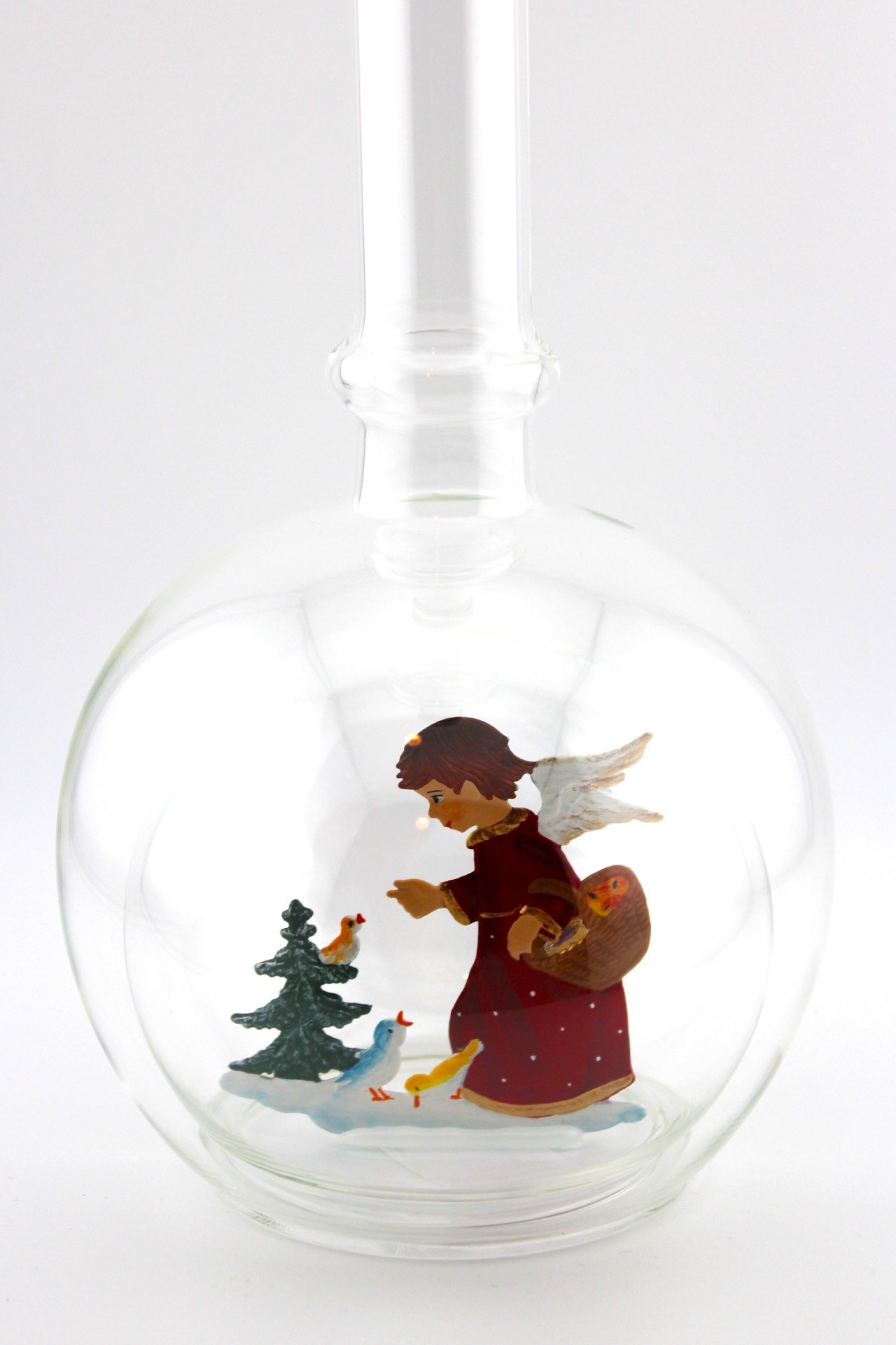 Eine leere bauchige Flasche aus Glas mit einem Vögel fütternden Engel am Tannenbaum im Inneren.