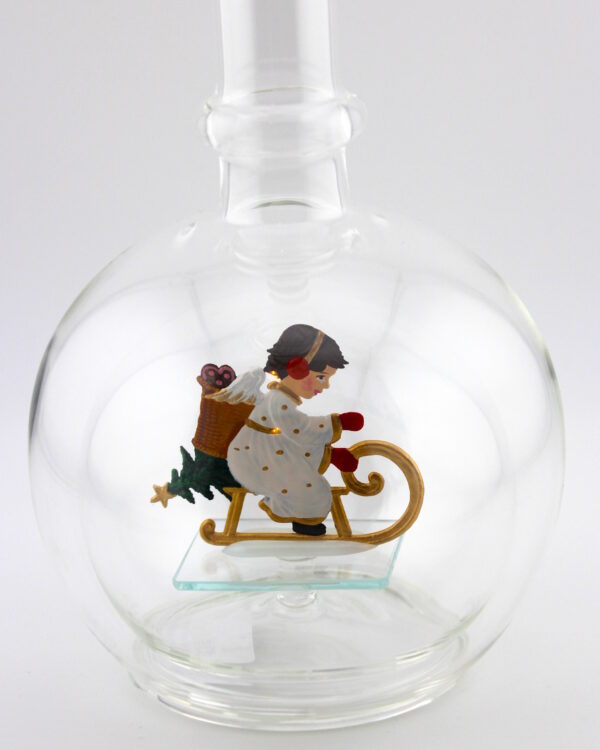 Eine leere bauchige Flasche aus Glas mit einem schlittenfahrenden Engel im Inneren.
