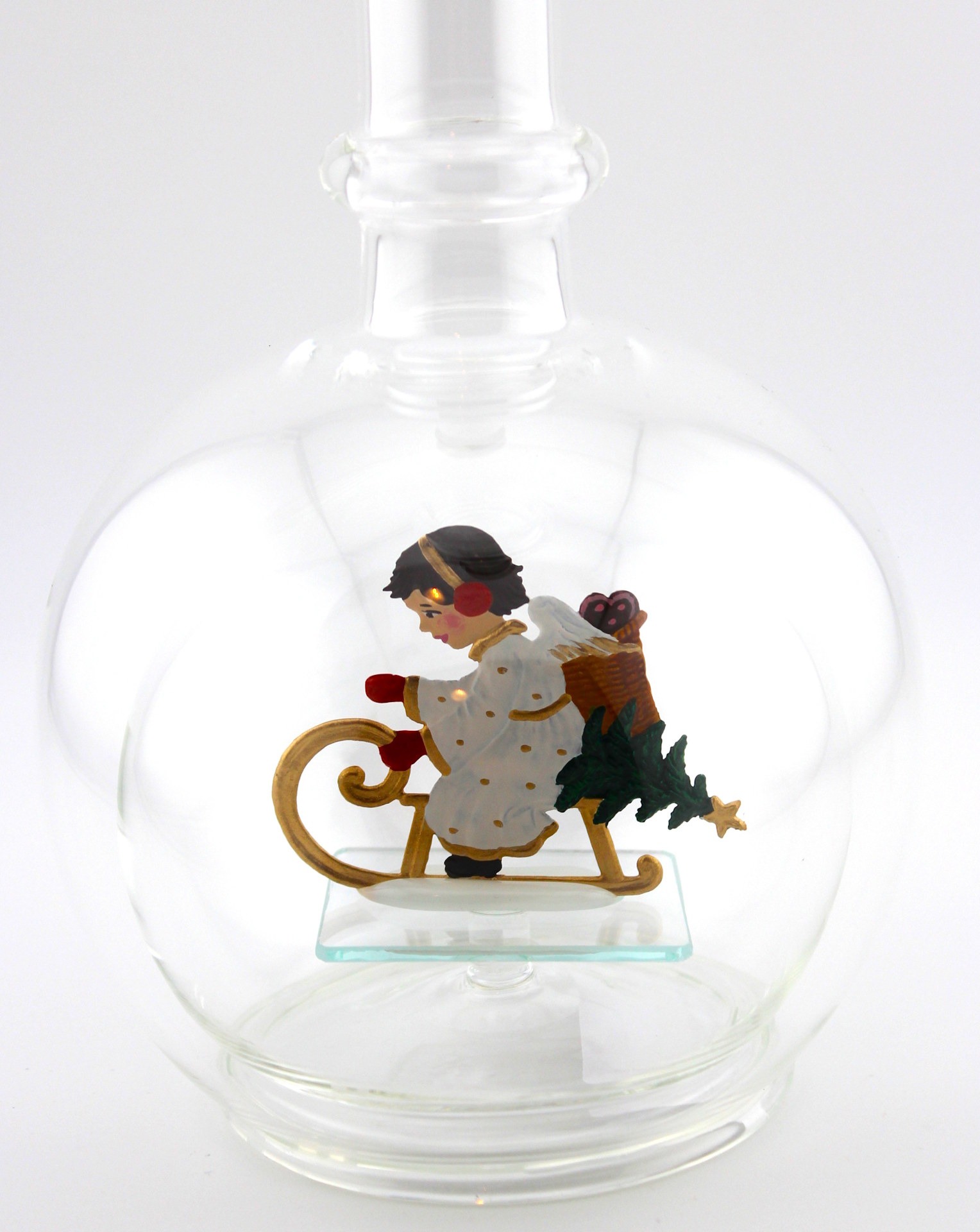 Eine leere bauchige Flasche aus Glas mit einem schlittenfahrenden Engel im Inneren.