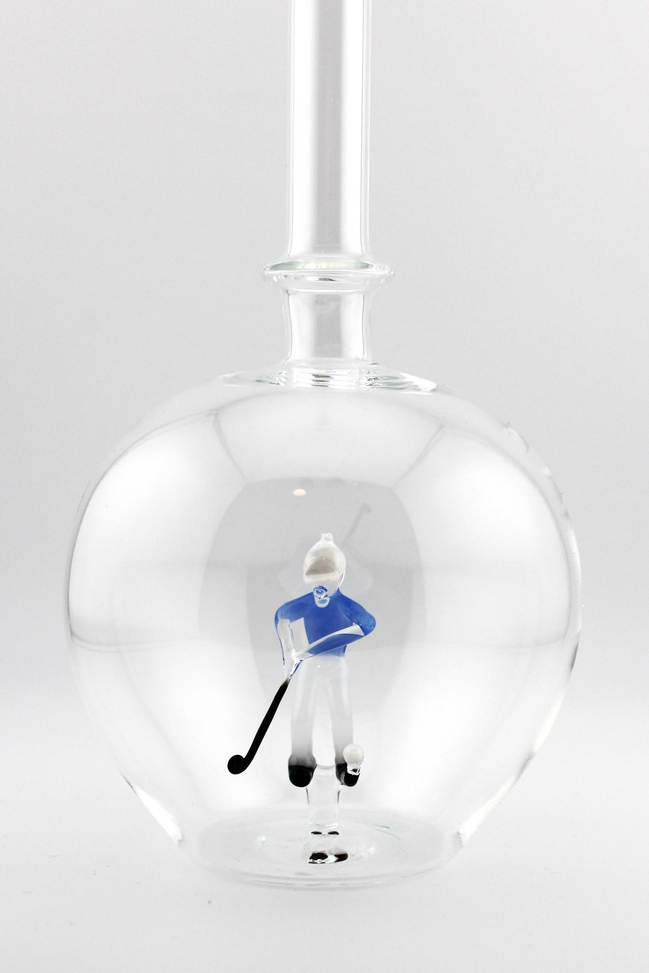 Eine leere bauchige Flasche aus Glas mit einem aus Glas geblasenen Golfspieler im Inneren.