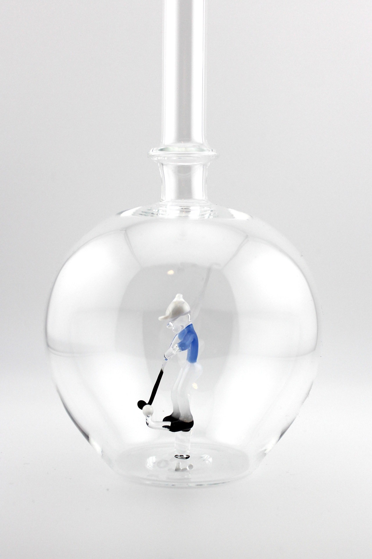 Eine leere bauchige Flasche aus Glas mit einem aus Glas geblasenen Golfspieler im Inneren.