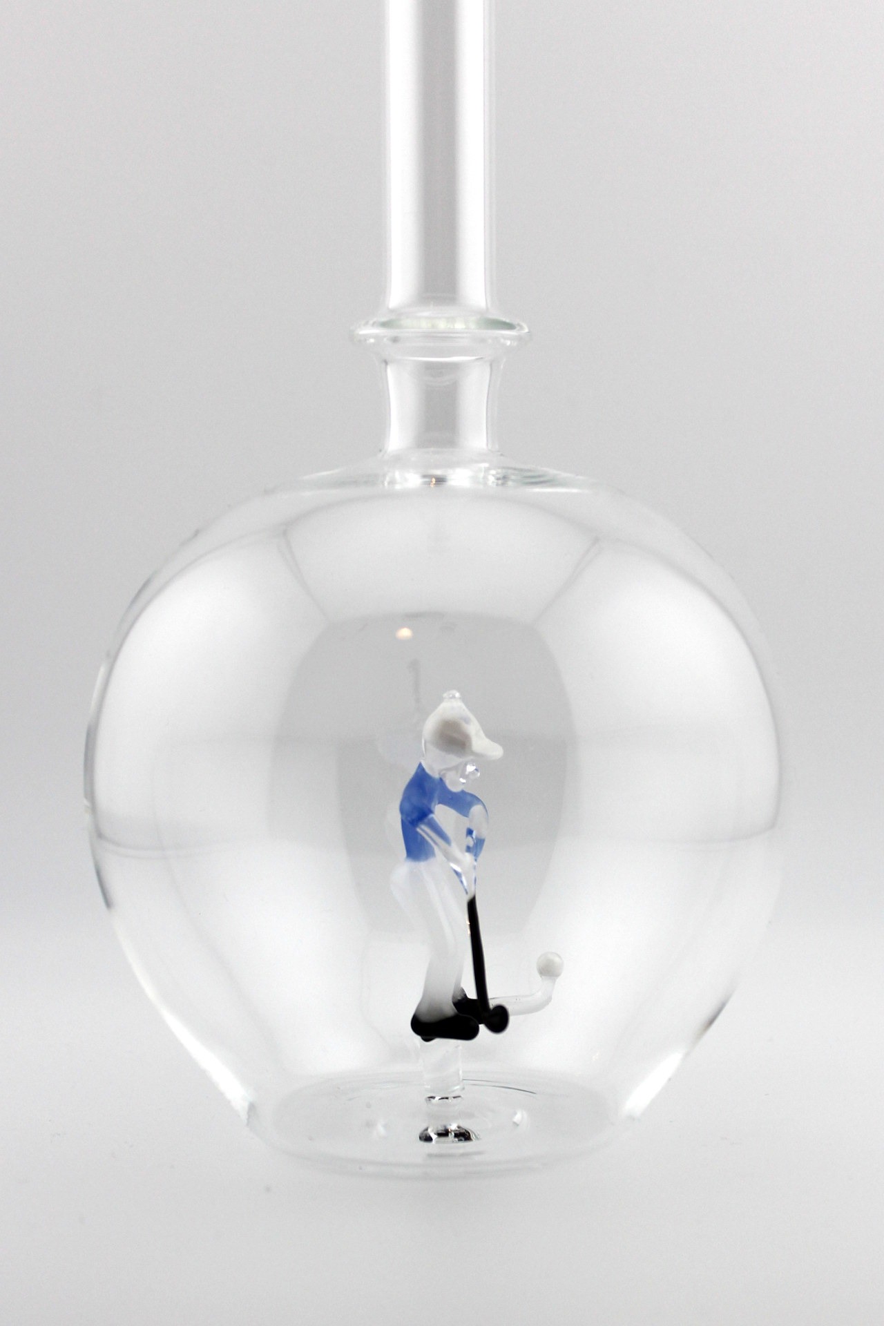 Eine leere bauchige Flasche aus Glas mit einem aus Glas geblasenen Golfspieler im Inneren.