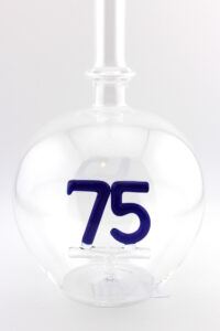 Eine leere bauchige Flasche aus Glas mit einer aus Glas geblasenen Zahl 75 im Inneren.
