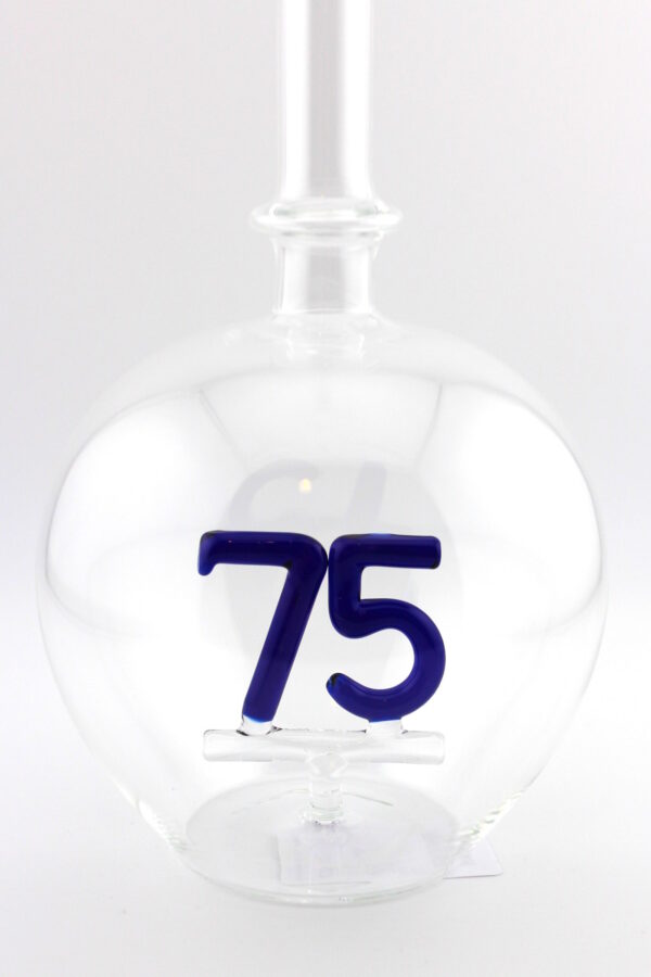 Eine leere bauchige Flasche aus Glas mit einer aus Glas geblasenen Zahl 75 im Inneren.